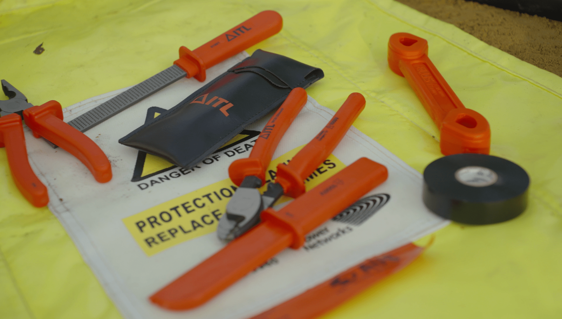 A VDE insulated tool kit laid out on a yellow high voltage warning sign with black electrical tape, ready for a line worker visual inspection.